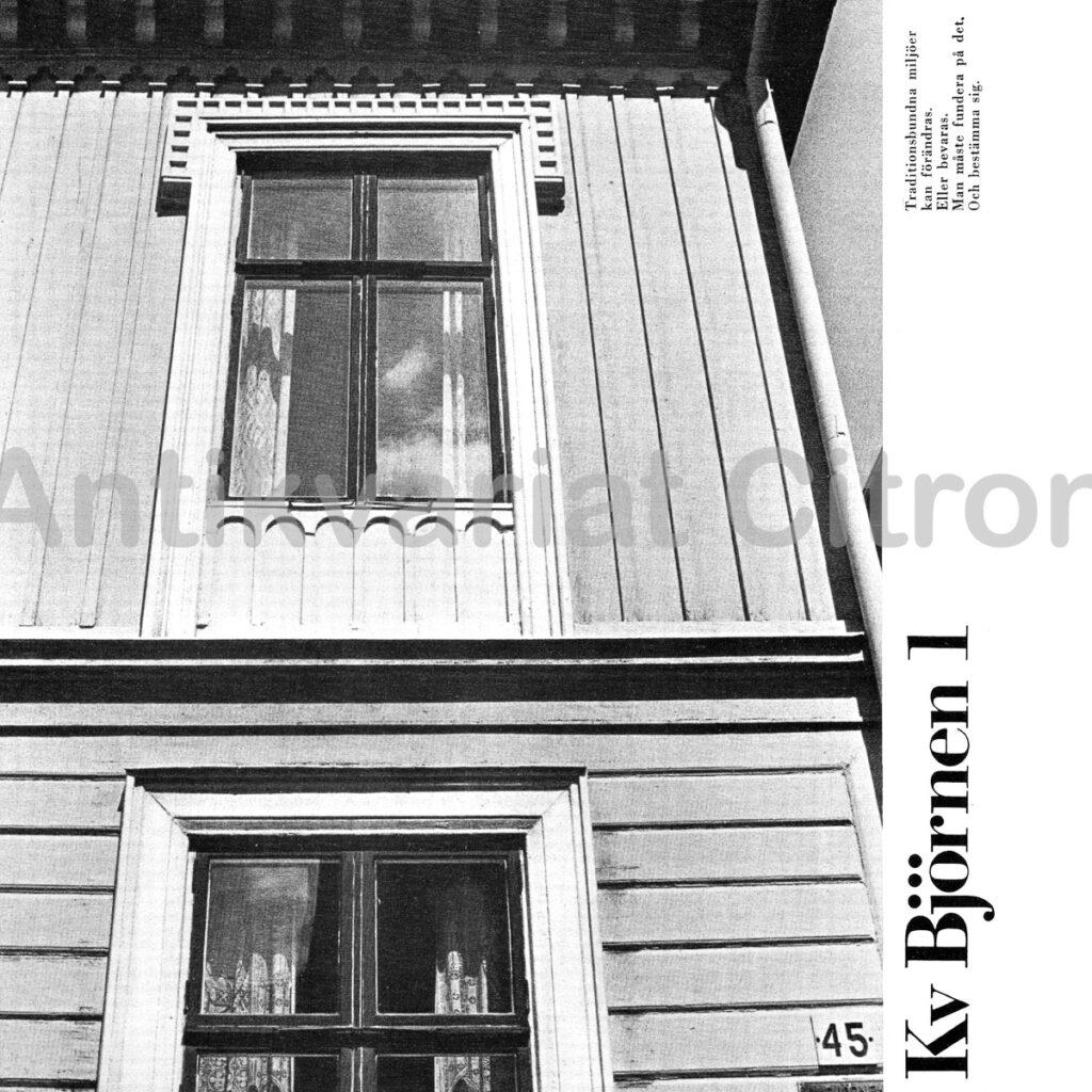 "Fasad till Björnen 1 – tvåvånings trähus med ljusgrå liggande panel, vitmålade fönsteromfattningar och enkel takfot. Dörren är klassiskt utformad med speglar och överljus, och flankeras av smala vertikala fönster. Byggnadens detaljer visar tydliga spår av 1800-talets formideal och ger ett hemtrevligt, tidlöst intryck."